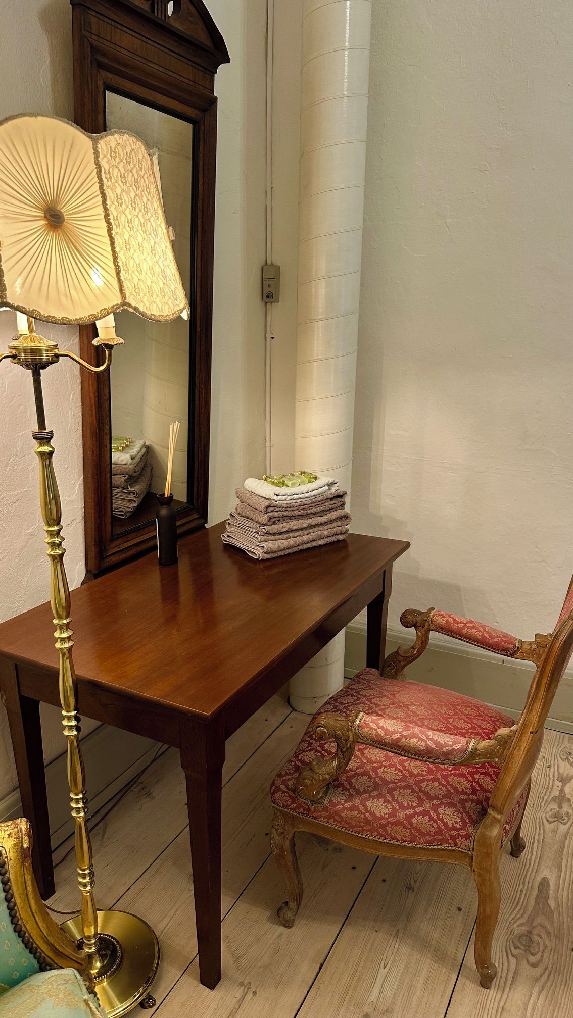 A wooden table with a lamp, a chair, and a stack of folded towels.