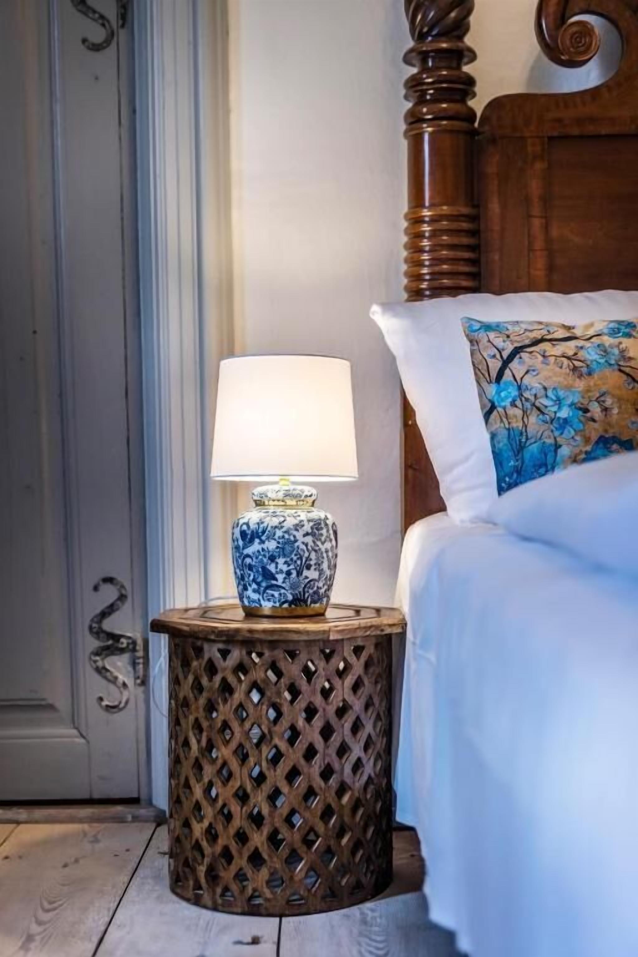 Ein Bett mit einem blumigen Kopfkissen, einer Nachttischlampe auf einem Holznachtisch und einem hölzernen Kopfteil.