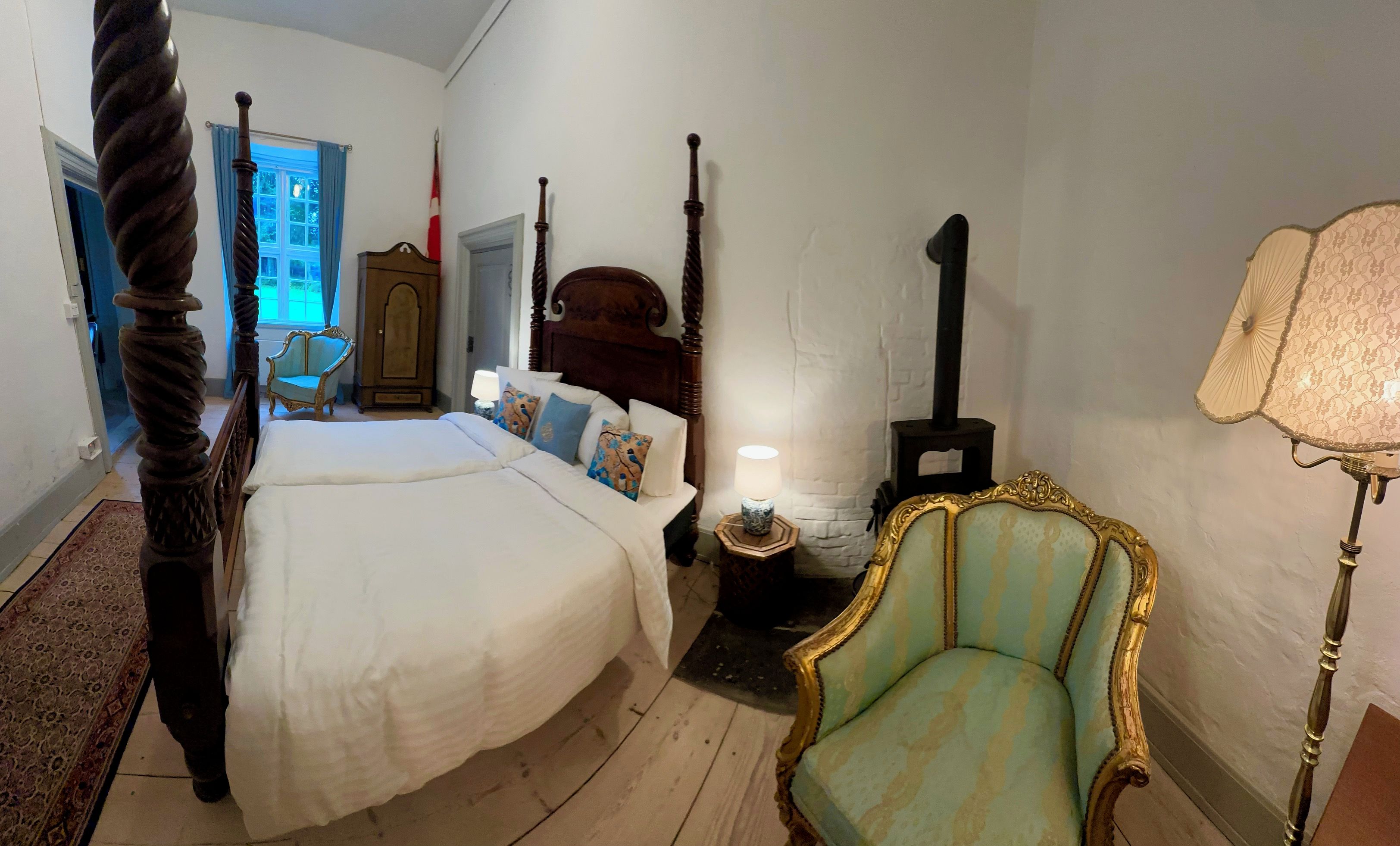 Un dormitorio con cama con dosel, una mesita de noche con lámpara, una silla y un armario.