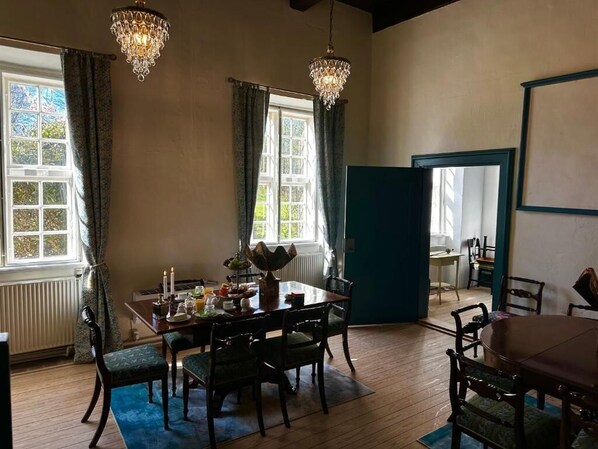 A dining area with a table set for four, two chandeliers, and a view through a window.