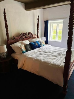 Uma cama de dossel com cabeceira de madeira, roupa de cama branca e almofadas decorativas.