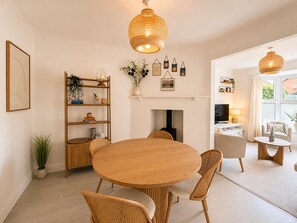 A dining area with a round wooden table, wicker chairs, a bookshelf, and a fireplace. - Rosemary House - Stylish home with garden in the heart of the South Downs (Petersfield)