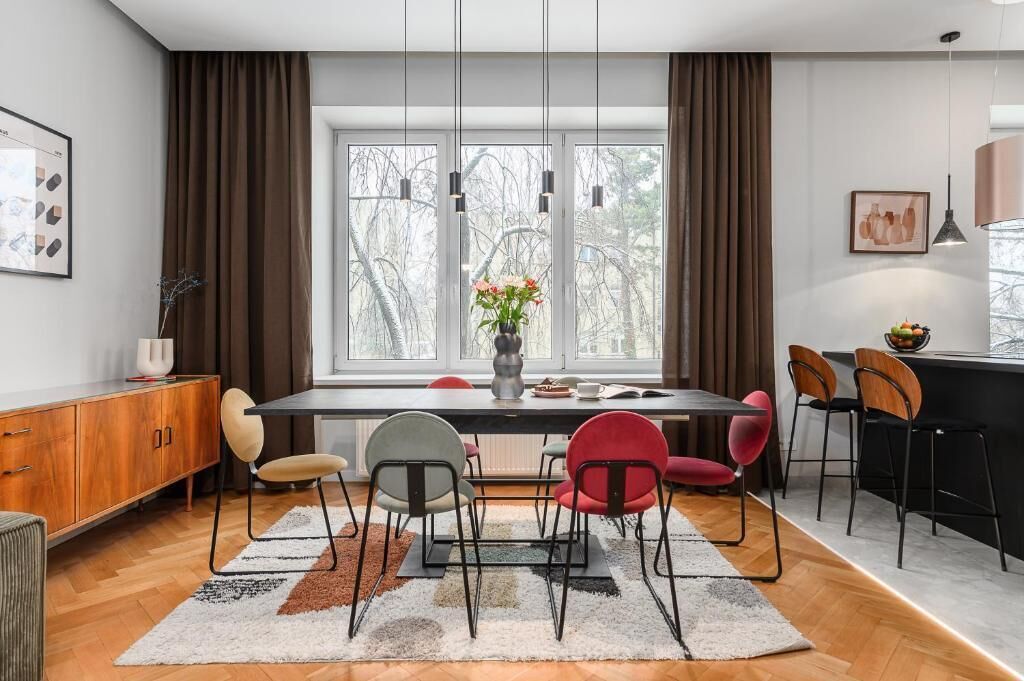 A modern dining area with a long table, multiple chairs, and a vase of flowers.