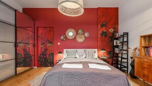 Ein Schlafzimmer mit einem Bett, einem Kleiderschrank, einem Nachttisch mit Lampe und einem Bücherregal.