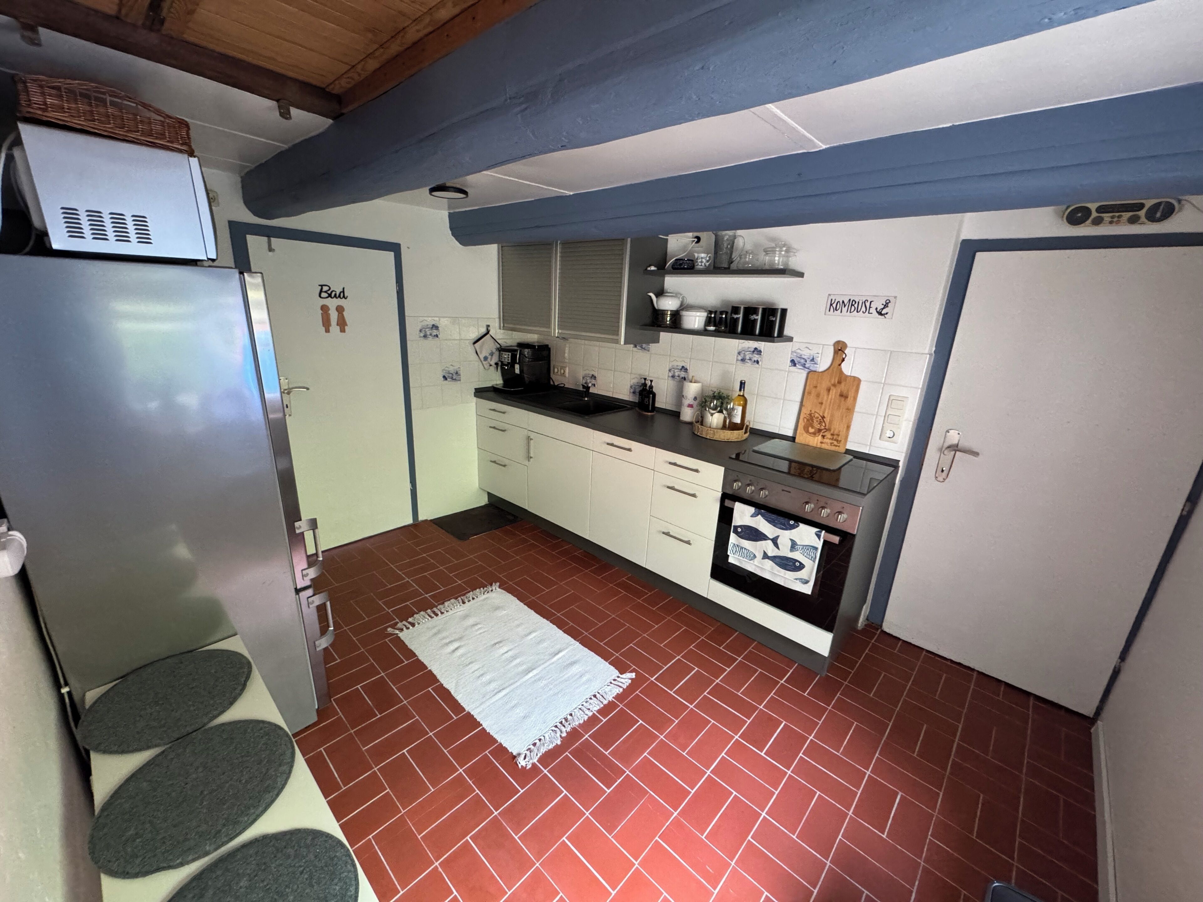 A compact kitchen with a refrigerator, stove, and cabinets, a tiled floor, and a wooden ceiling.