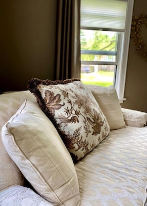 Una cama con un cojín floral y una ventana con vista a follaje.