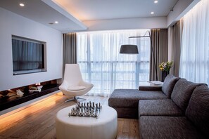 A modern living room with a flat-screen TV, a white chair, a gray sofa, a chessboard, and a large window with curtains. - Citta Residences Hengfeng (Shanghai)