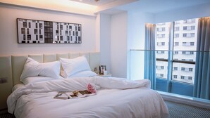 Quarto de hotel com cama, mesa de cabeceira, quadro emoldurado, janela com cortinas e vista para a cidade.