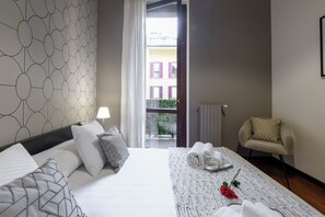 A hotel room with a bed, a chair, a table with towels, and a view of buildings outside. - Borromei 11  Eleganza in pieno centro (Milano)