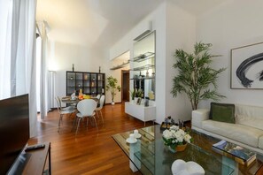 A modern living room with a glass coffee table, white sofa, and a dining area with chairs and a table. - Borromei 11  Eleganza in pieno centro (Milano)