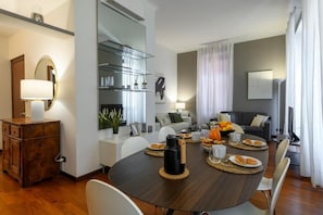 A modern living room with a dining table set for breakfast, a sofa, a coffee table, and a TV. - Borromei 11  Eleganza in pieno centro (Milano)