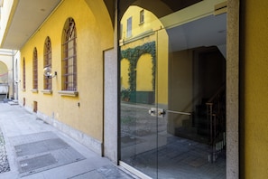 A building with arched windows and a glass door, a paved walkway, and a visible staircase. - Borromei 11  Eleganza in pieno centro (Milano)