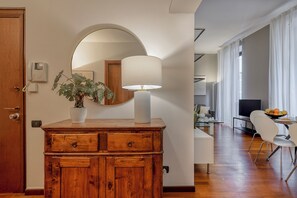 A wooden dresser with a lamp, a potted plant, and a mirror in a room with a dining area visible in the background. - Borromei 11  Eleganza in pieno centro (Milano)