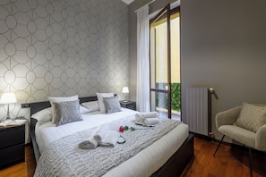 A hotel room with a bed, two bedside tables with lamps, a chair, a window with curtains, and a view of greenery outside. - Borromei 11  Eleganza in pieno centro (Milano)
