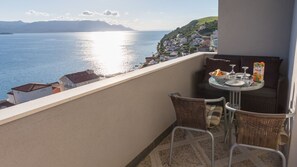 Ein Balkon mit Korbstühlen, einem kleinen Tisch mit Obstschale, Weingläsern und einer Saftpackung.