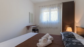 Ein Hotelzimmer mit Bett, Schreibtisch, Stuhl, einem Fenster mit durchsichtigen Vorhängen und einer Nachttischlampe.