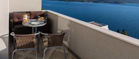 Ein Balkon mit Korbstühlen, einem Tisch für zwei Personen und Blick auf einen See und Hügel.