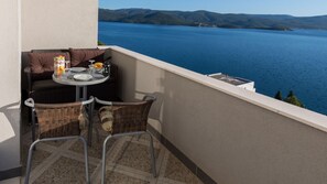 Ein Balkon mit Korbstühlen, einem Tisch für zwei Personen und Blick auf einen See und Hügel.