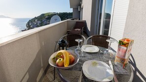 A balcony with a table set for two, a bowl of fruit, a glass of water, and a carton of juice. - Apartman Arapovic 5 by Villas Guide (Klek)