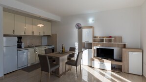 A modern kitchen with a dining area, a TV, and a clock on the wall. - Apartman Arapovic 4 by Villas Guide (Klek)