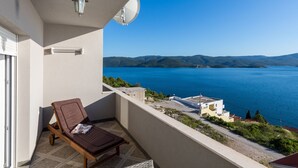 A balcony with a brown lounge chair, a satellite dish, and a view of a lake with buildings and hills in the distance. - Apartman Arapovic 4 by Villas Guide (Klek)