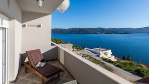 Ein Balkon mit braunem Liegestuhl, einer Satellitenschüssel und Blick auf einen See mit Gebäuden und Hügeln im Hintergrund.