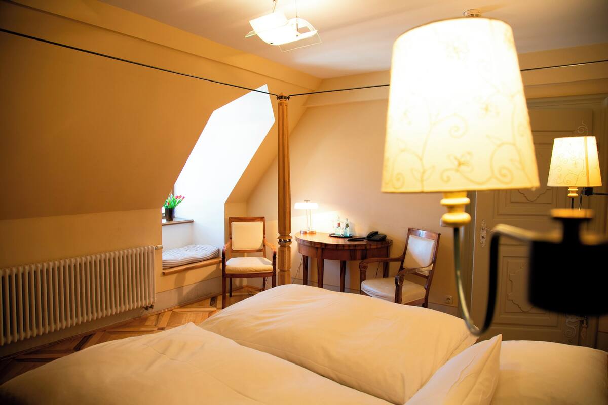 A hotel room with a bed, two chairs, a table, and a lamp.