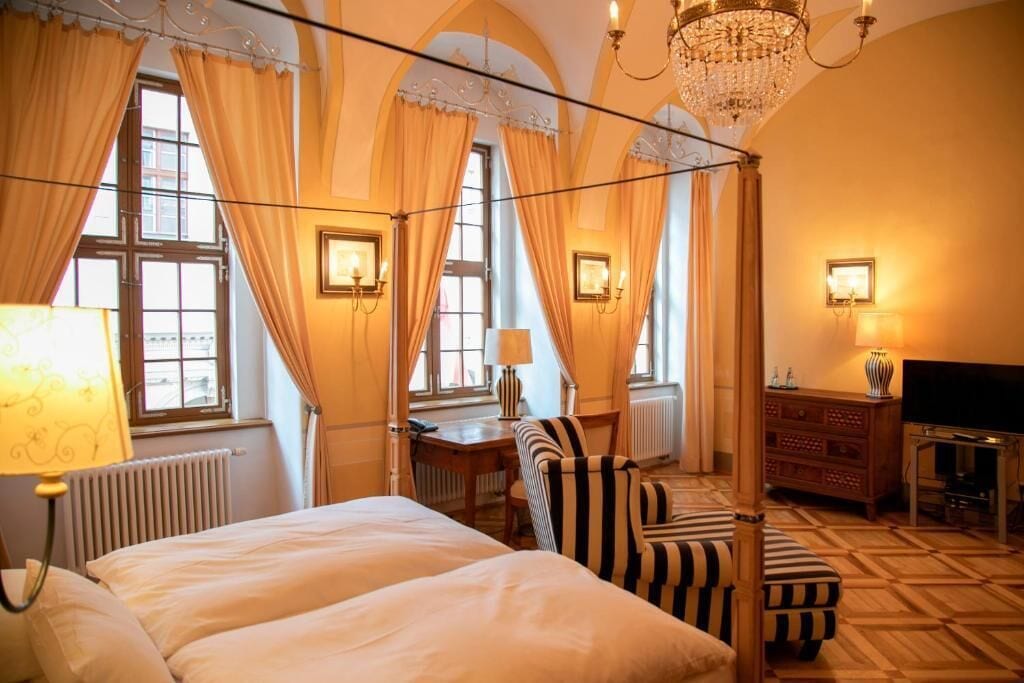 A hotel room with a four-poster bed, a desk, a television, and a chandelier.
