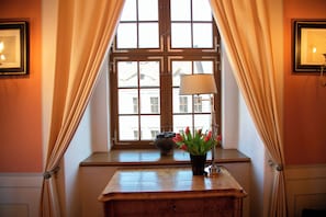 Una habitación con un amplio ventanal, un escritorio con lámpara y un jarrón con flores.