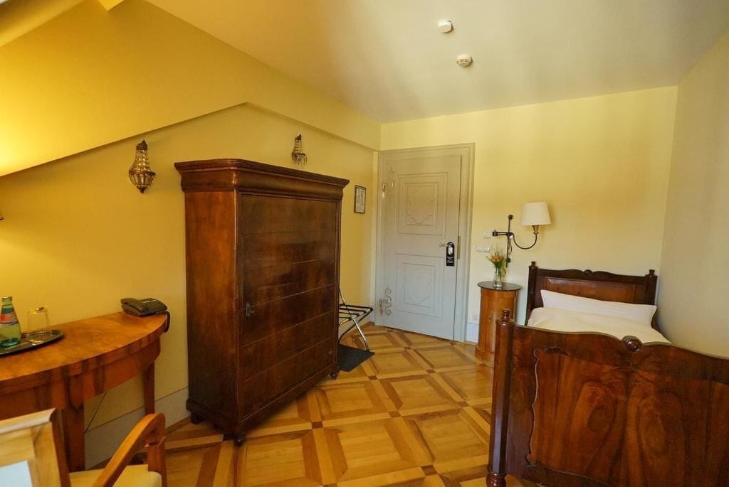 Une pièce comprenant un lit en bois, une commode en bois, une table  à manger avec des chaises, une lampe et une porte.