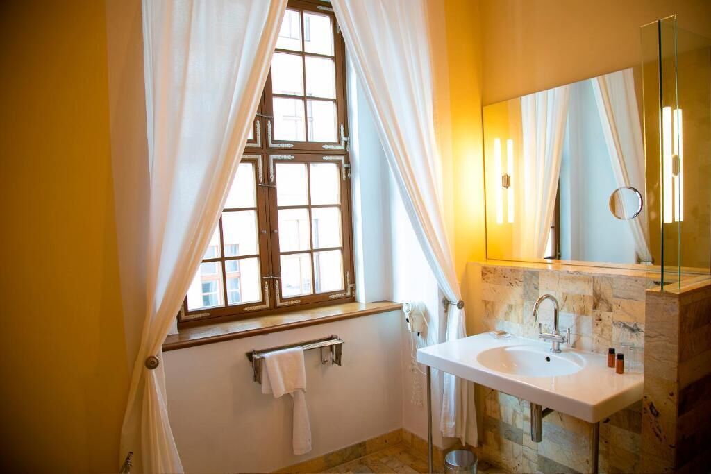 Een badkamer met een raam, een wastafel, een spiegel en een handdoekhouder.