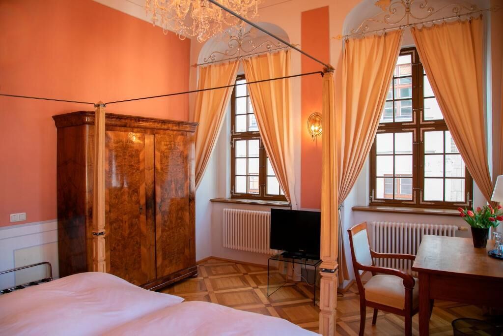 Una habitación con cama, un armario de madera, un escritorio con silla, televisión y ventana con cortinas.