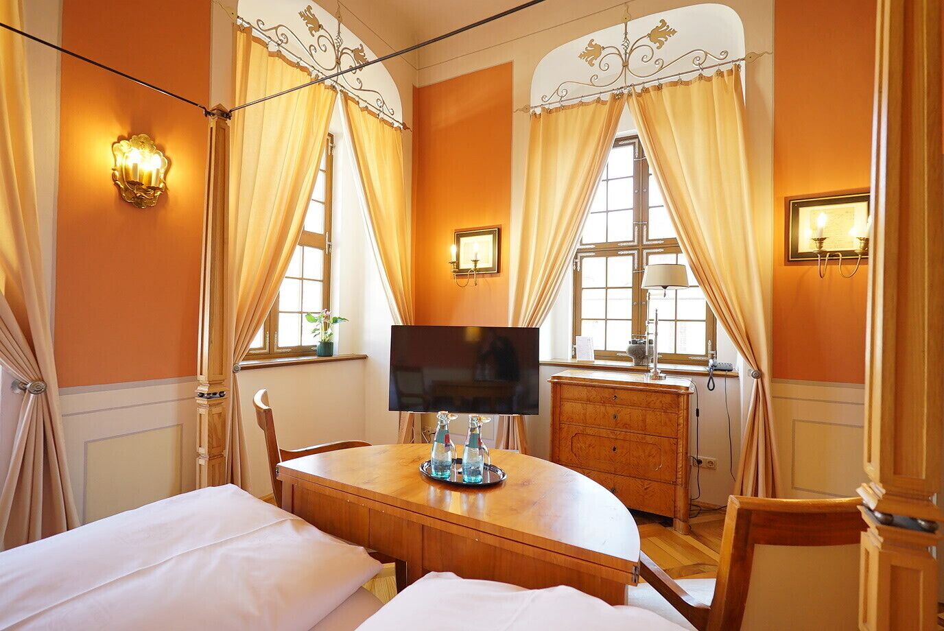 A hotel room with a bed, a TV, a wooden table, and a window with curtains.