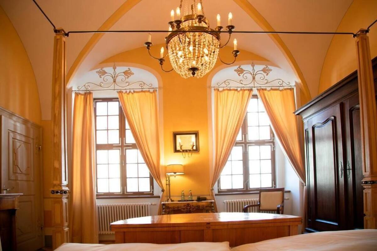 A room with a chandelier, a bed, a table, and a radiator.