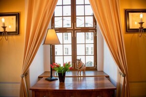 Una habitación con un ventanal grande, un escritorio con lámpara, un florero con flores y una figura decorativa de caballo.