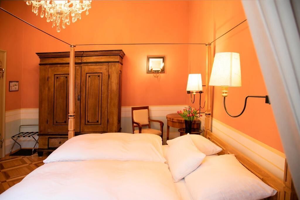 Ein Hotelzimmer mit einem Bett, einem Holzschrank, zwei Wandlampen, einem Sessel und einem kleinen Tisch mit Blumen.