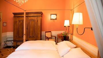 Ein Hotelzimmer mit einem Bett, einem Holzschrank, zwei Wandlampen, einem Sessel und einem kleinen Tisch mit Blumen.