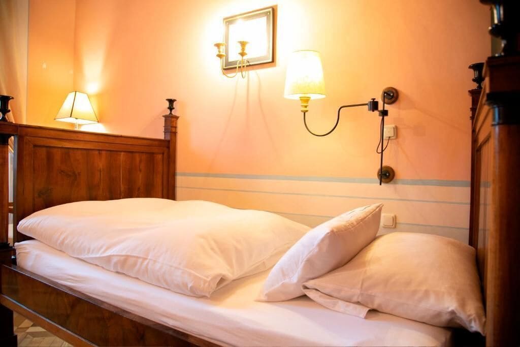 A single bed with white bedding in a room with wooden headboard and a wall-mounted light fixture.