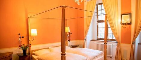 Una cama con dosel en una habitación con paredes anaranjadas, un candelabro y una ventana con cortinas.