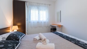 Ein Hotelzimmer mit Bett, Schreibtisch, Stuhl, einem Fenster mit durchsichtigen Vorhängen und einem Spiegel an der Wand.