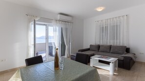 Ein Wohnzimmer mit einer Couch, einem Couchtisch und einem Esstisch, auf dem eine Flasche und ein Glas stehen.