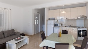 A modern kitchen with white appliances, a dining table with chairs, and a grey sofa in a bright living area. - Apartman Arapovic 2 by Villas Guide (Klek)