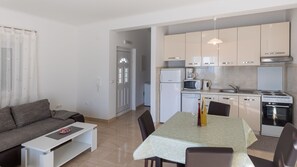 A modern kitchen with white appliances, a dining table with chairs, and a grey sofa in a bright living area. - Apartman Arapovic 2 by Villas Guide (Klek)