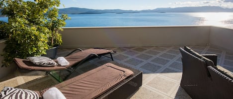 A balcony with two sun loungers, a wicker sofa, and a potted plant.