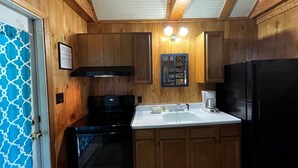 Una cocina con armarios de madera, una estufa negra, un lavaplatos y un refrigerador.