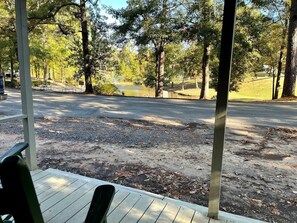 A covered outdoor area with a wooden deck, a paved path, and a body of water in the background.