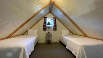 A small, triangular attic bedroom with two single beds, a window with curtains, and a lamp.