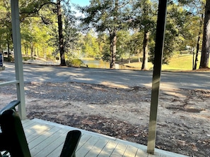 A covered outdoor area with a wooden deck, a paved path, and a body of water in the background.