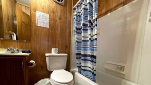 Un baño con tocador de madera, inodoro, ducha con cortina a rayas y bañera blanca.