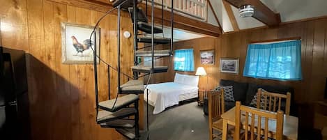 A wooden interior with a spiral staircase, a bed, a table, and a sofa.